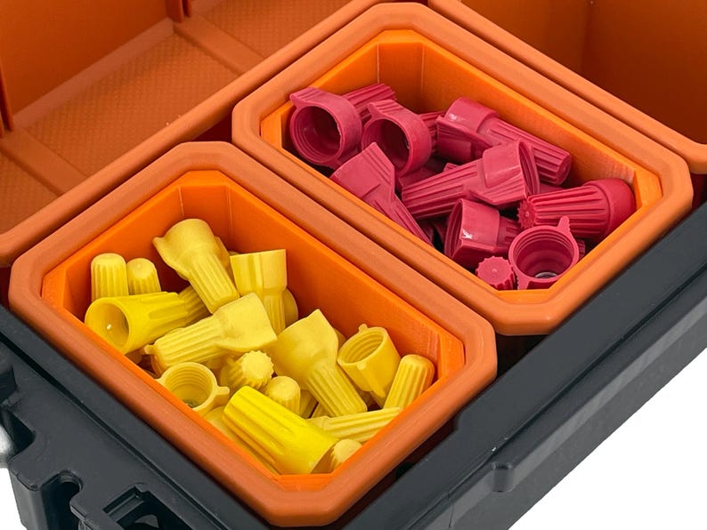 Puede incluir: Una caja de almacenamiento de pl&aacute;stico negro con dos compartimentos naranjas llenos de conectores de alambre rojos y amarillos.