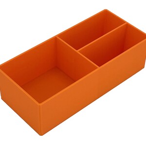 May include: An orange rectangular organiser with three compartments. The organiser is made of a solid material and is designed to hold small items. The compartments are divided by vertical walls.