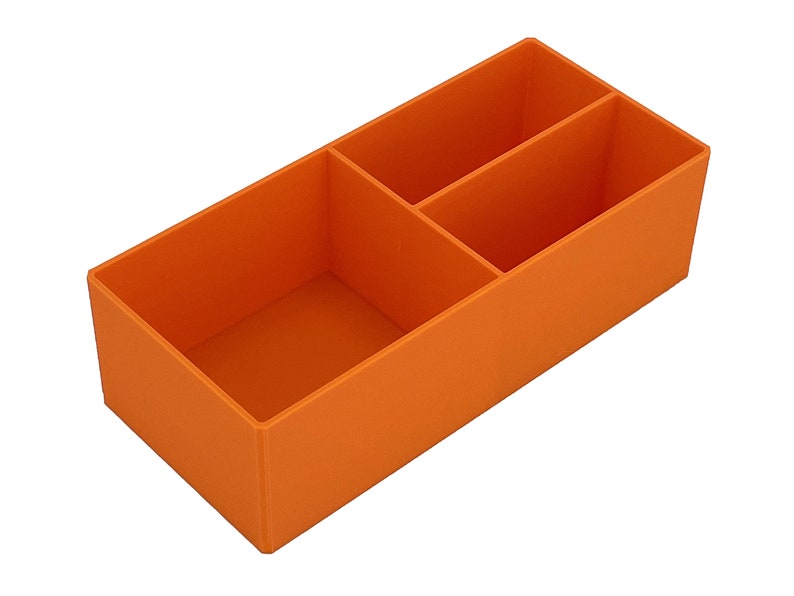 May include: An orange rectangular organiser with three compartments. The organiser is made of a solid material and is designed to hold small items. The compartments are divided by vertical walls.