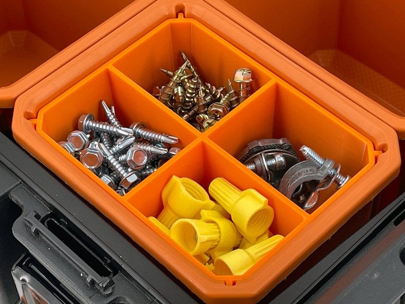 May include: An orange and black toolbox with an orange interior divided into four compartments. The compartments contain various hardware items, including screws, wire connectors, and other fasteners.