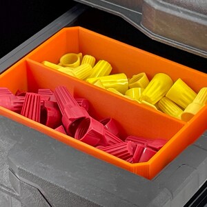 May include: An orange plastic organizer with two compartments, filled with red and yellow wire connectors. The organizer is inside a dark gray toolbox, providing a clear view of the electrical components.