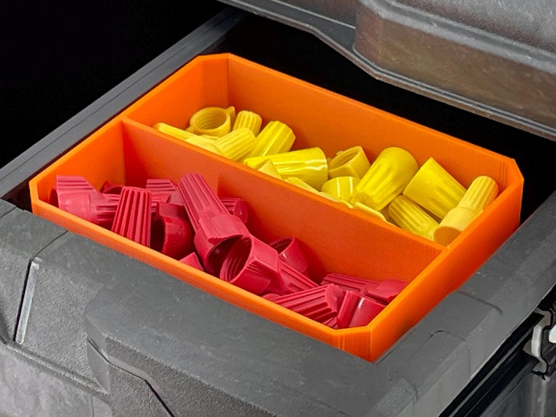 May include: An orange plastic organizer with two compartments, filled with red and yellow wire connectors. The organizer is inside a dark gray toolbox, providing a clear view of the electrical components.