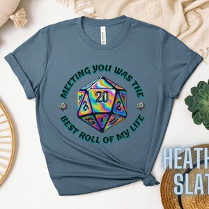 May include: A blue t-shirt with a graphic of a rainbow iridescent 20-sided die with the text "Meeting you was the best roll of my life".