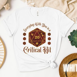 May include: White t-shirt with a red and gold 20-sided die graphic and the text "Everyday With You is a Critical Hit".