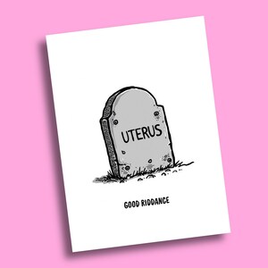 May include: A white greeting card featuring a black and white line drawing of a grey tombstone with the word UTERUS written on it. Below the tombstone, the text GOOD RIDDANCE is printed in black capital letters on the white card surface.