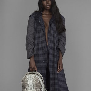 Pode incluir: Uma mulher vestindo um casaco longo estampado em azul escuro e cinza com uma mochila de couro de cobra.