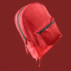 Pode incluir: Uma mochila de couro vermelha com um bolso com z&iacute;per e um efeito de gotejamento. A mochila &eacute; feita de um material texturizado e tem um z&iacute;per preto.