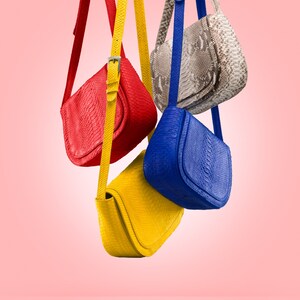 May include: Four different coloured leather handbags hanging from a pink background. The bags are red, blue, yellow, and a light brown with a snakeskin pattern.