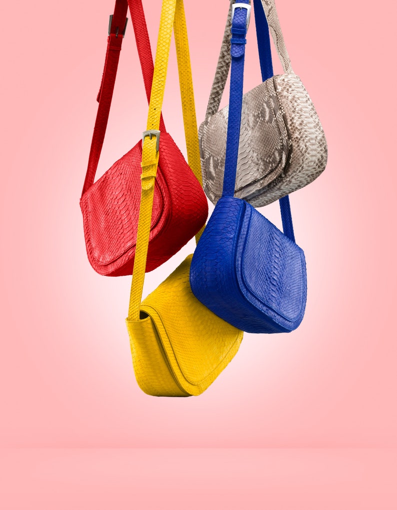 May include: Four different coloured leather handbags hanging from a pink background. The bags are red, blue, yellow, and a light brown with a snakeskin pattern.