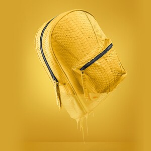 Pode incluir: Uma mochila de couro amarela com um bolso com z&iacute;per e puxadores de z&iacute;per pretos. A mochila est&aacute; pingando tinta amarela.