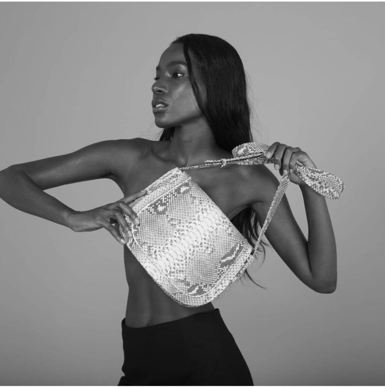 Pode incluir: Uma bolsa de ombro de pele de cobra preta e branca com uma al&ccedil;a longa. A bolsa est&aacute; sendo usada por uma pessoa com cabelo preto comprido.