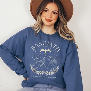 May include: Indigo blue sweatshirt with the word "BASGIATH" and a graphic of a dragon, mountains, and a castle. The text "In the years of peace we find our greatest courage" is below the graphic.