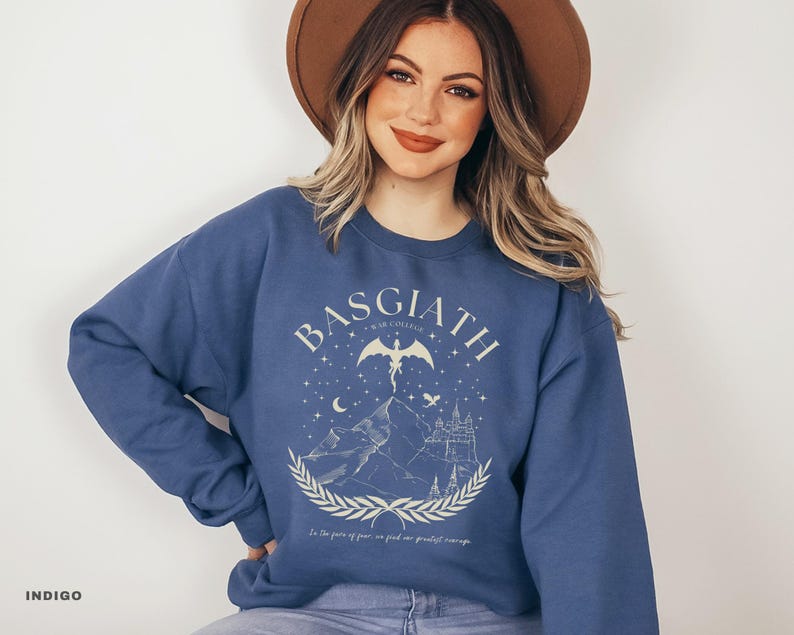 May include: Indigo blue sweatshirt with the word "BASGIATH" and a graphic of a dragon, mountains, and a castle. The text "In the years of peace we find our greatest courage" is below the graphic.