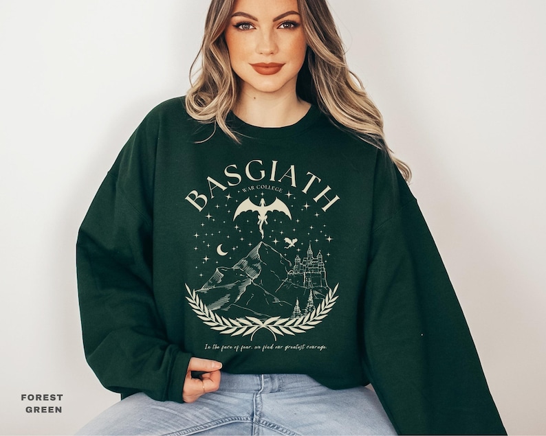 May include: Forest green sweatshirt with a graphic design featuring the word "BASGIATH", a winged creature, mountains, a castle, and the text "In the face of fear, we find our greatest courage."