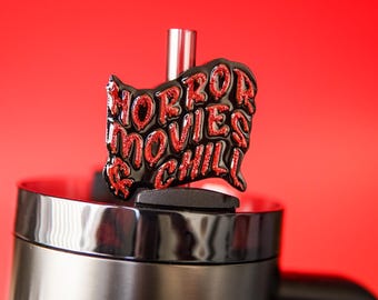 May include: A black enamel pin shaped like the state of Ohio featuring the red glitter text HORROR MOVIES & CHILL. The pin is attached to the lid of a black travel mug with a silver straw protruding from the center against a red background.