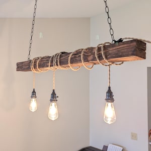 May include: A rustic, wooden beam chandelier with three Edison-style light bulbs. The beam is wrapped with rope and suspended from the ceiling by black chains. The light fixtures hang over a piano.