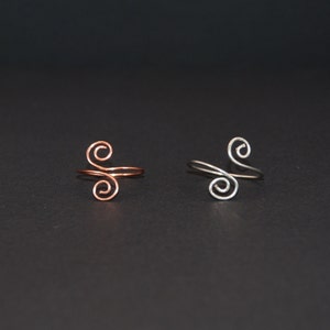 Op de afbeelding: Twee eenvoudige ringen met een dubbel spiraalontwerp. De ene ring is van koper en de andere van zilver.