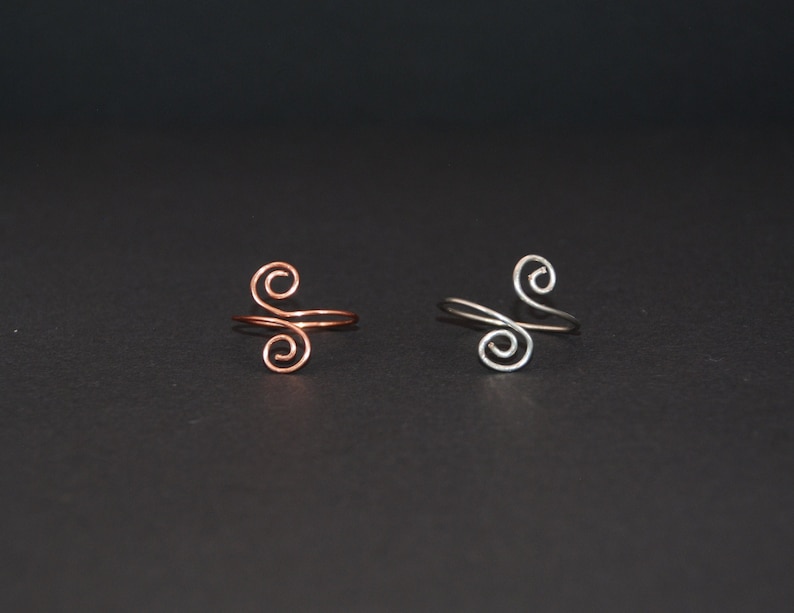 Op de afbeelding: Twee eenvoudige ringen met een dubbel spiraalontwerp. De ene ring is van koper en de andere van zilver.