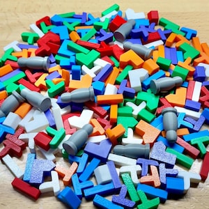 May include: A pile of colorful, geometric puzzle pieces in various shapes and sizes. The pieces are primarily red, green, blue, orange, and white, with a few gray cylindrical pieces scattered throughout. The pieces are made of plastic.