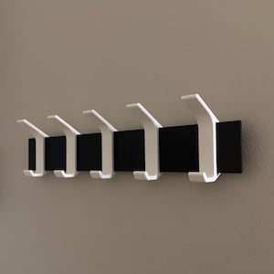 May include: A black metal wall-mounted coat rack with five white plastic hooks.