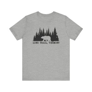 May include: A grey t-shirt with a black graphic of a bear walking in front of a forest of pine trees. The text "LONG TRAIL, VERMONT" is printed below the graphic in a serif font.
