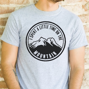 May include: A gray t-shirt with a black and white graphic of two mountains. The graphic is a circle with the text "I spent a little time on the mountain" around the mountains.