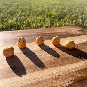 May include: Five small, brown, ceramic figurines with painted faces and yellow accents. The figurines are arranged in a row on a wooden surface.