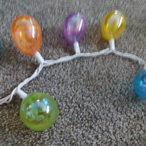 May include: A string of iridescent pastel colored globe lights with white wires. The lights are in a variety of colors including blue, green, yellow, orange, and purple.