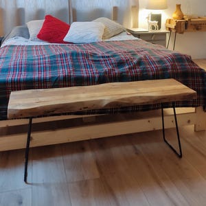 Könnte beinhalten: Eine Holzbank mit schwarzen Metall-Haarnadelbeinen steht am Fuß eines Bettes. Das Bett hat eine karierte Decke in Grün, Rot und Blau. Weiße und rote Kissen liegen auf dem Bett. Ein Nachttisch und eine Lampe sind sichtbar.