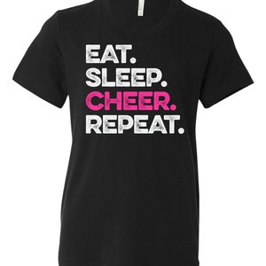 Könnte beinhalten: Schwarzes T-Shirt mit dem Text "EAT. SLEEP. CHEER. REPEAT." in Weiß und Pink. Das Shirt hat einen Rundhalsausschnitt und kurze Ärmel. Der Text ist in einer fetten, verwaschenen Schrift.