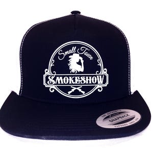 Puede incluir: Gorra de camionero negra y blanca con un logotipo blanco que dice "Small Town Smokeshow" con una silueta de una mujer con un sombrero de vaquero. El logotipo está dentro de un círculo con un borde decorativo. La gorra tiene una malla blanca en la parte posterior y una visera negra.