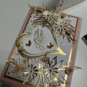 Könnte beinhalten: Eine weiße Karte mit einem goldenen Herzen und floralem Design. Das Herz trägt den Text "Von ganzem Herzen" in goldenen Lettern.
