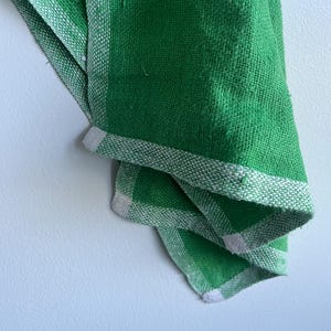 Pu&ograve; includere: Un asciugamano da cucina verde con strisce bianche. L'asciugamano &egrave; piegato e appeso a un muro bianco.