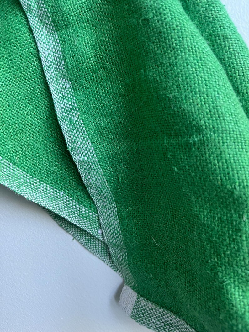 Pu&ograve; includere: Primo piano di un tessuto verde con un bordo bianco. Il tessuto ha una trama tessuta ed &egrave; piegato.