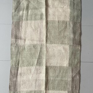 Puede incluir: Una manta de tiro a cuadros verde y beige con textura tejida.