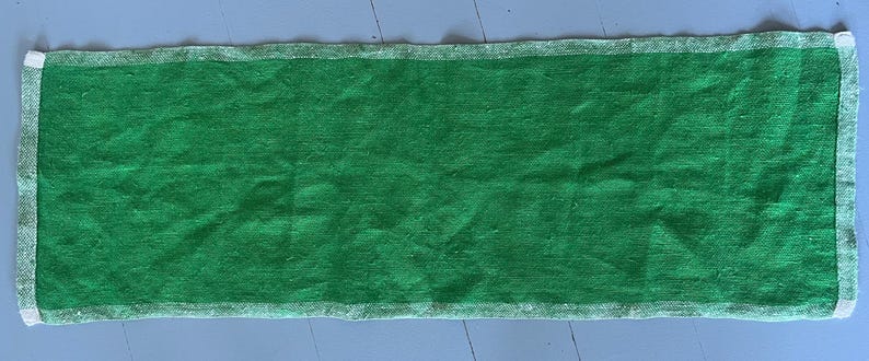 Pu&ograve; includere: Un runner da tavolo in lino verde con bordi bianchi. Il runner &egrave; largo circa 46 cm e lungo 122 cm.