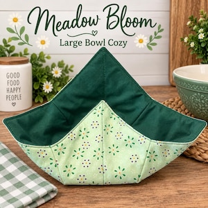 May include: A large bowl cozy featuring a light green exterior fabric with a repeating pattern of small white and yellow flowers. The interior is a solid dark green fabric. The cozy has a square, quilted design with pointed corners.