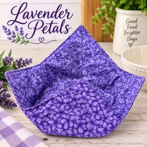 May include: A fabric bowl cozy featuring a vibrant purple floral pattern with quilted stitching. The interior and exterior display a repeating design of small purple flowers and leaves. The square-shaped holder has four pointed corners.