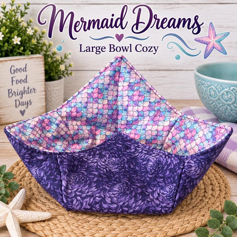 May include: A large bowl cozy featuring a reversible design. The interior fabric displays a pink, purple, and blue mermaid scale pattern. The exterior fabric is a dark purple with a floral print. The text Mermaid Dreams Large Bowl Cozy is visible.