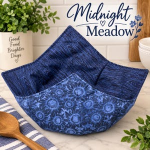 May include: A fabric bowl cozy featuring a dark blue wood grain pattern on the interior and a blue sunflower print on the exterior. The square-shaped quilted holder has four pointed corners and is constructed with visible stitching throughout.