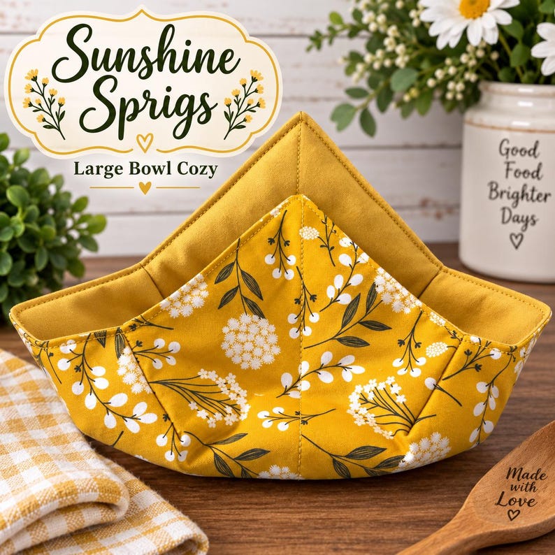 May include: A large bowl cozy featuring a mustard yellow fabric with a white floral sprig pattern and a solid mustard yellow interior. The item is labeled Sunshine Sprigs Large Bowl Cozy with a decorative graphic and text on the fabric.