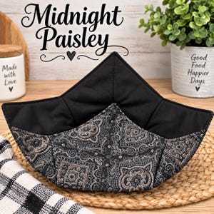 May include: A fabric bowl cozy featuring a black and grey paisley pattern on the exterior and a solid black interior. The square-shaped holder has four pointed corners and is constructed with quilted stitching throughout the fabric panels.