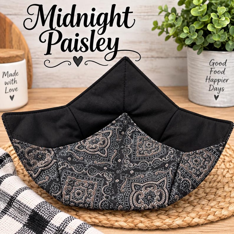 May include: A fabric bowl cozy featuring a black and grey paisley pattern on the exterior and a solid black interior. The square-shaped holder has four pointed corners and is constructed with quilted stitching throughout the fabric panels.