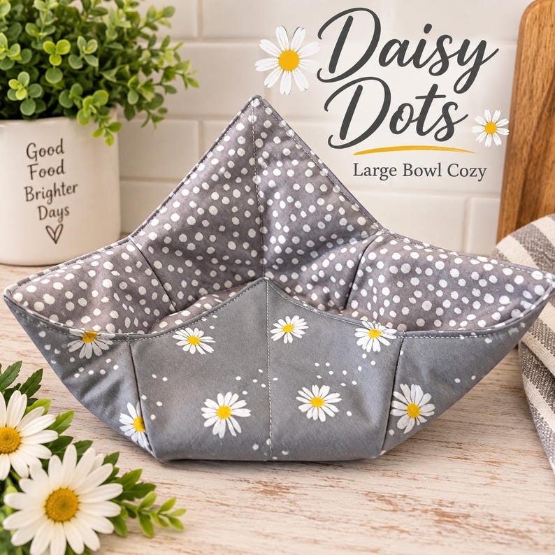 May include: A large bowl cozy featuring a gray exterior with a white daisy floral pattern and a gray interior lining with a white polka dot pattern. The fabric item is shaped with four corners and includes text that reads Daisy Dots Large Bowl Cozy.