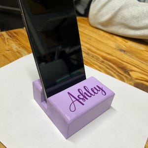 May include: A lavender wooden phone stand with the name "Ashley" engraved in purple lettering.