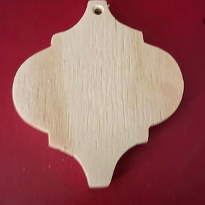 Puede incluir: Un adorno de madera de color marrón claro sin decoración, con un agujero en la parte superior para colgar. El adorno tiene forma de lágrima con la parte superior redondeada y la inferior puntiaguda.