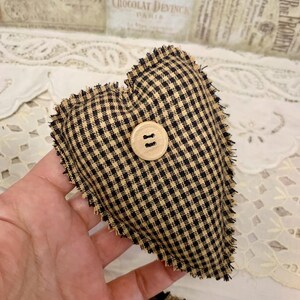 May include: A black and tan gingham heart-shaped pillow with a wooden button in the center. The pillow has a frayed edge.