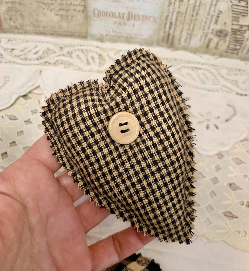 May include: A black and tan gingham heart-shaped pillow with a wooden button in the center. The pillow has a frayed edge.