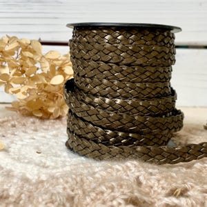 May include: A spool of metallic bronze braided cord featuring a tight, uniform weave pattern. The cord is wound in multiple layers around a central black cylindrical core, displaying a consistent dark, shimmering finish throughout the entire length.