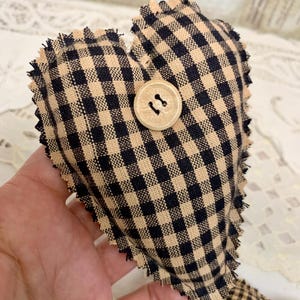 May include: A black and tan gingham heart-shaped pillow with a wooden button. The pillow has a frayed edge.